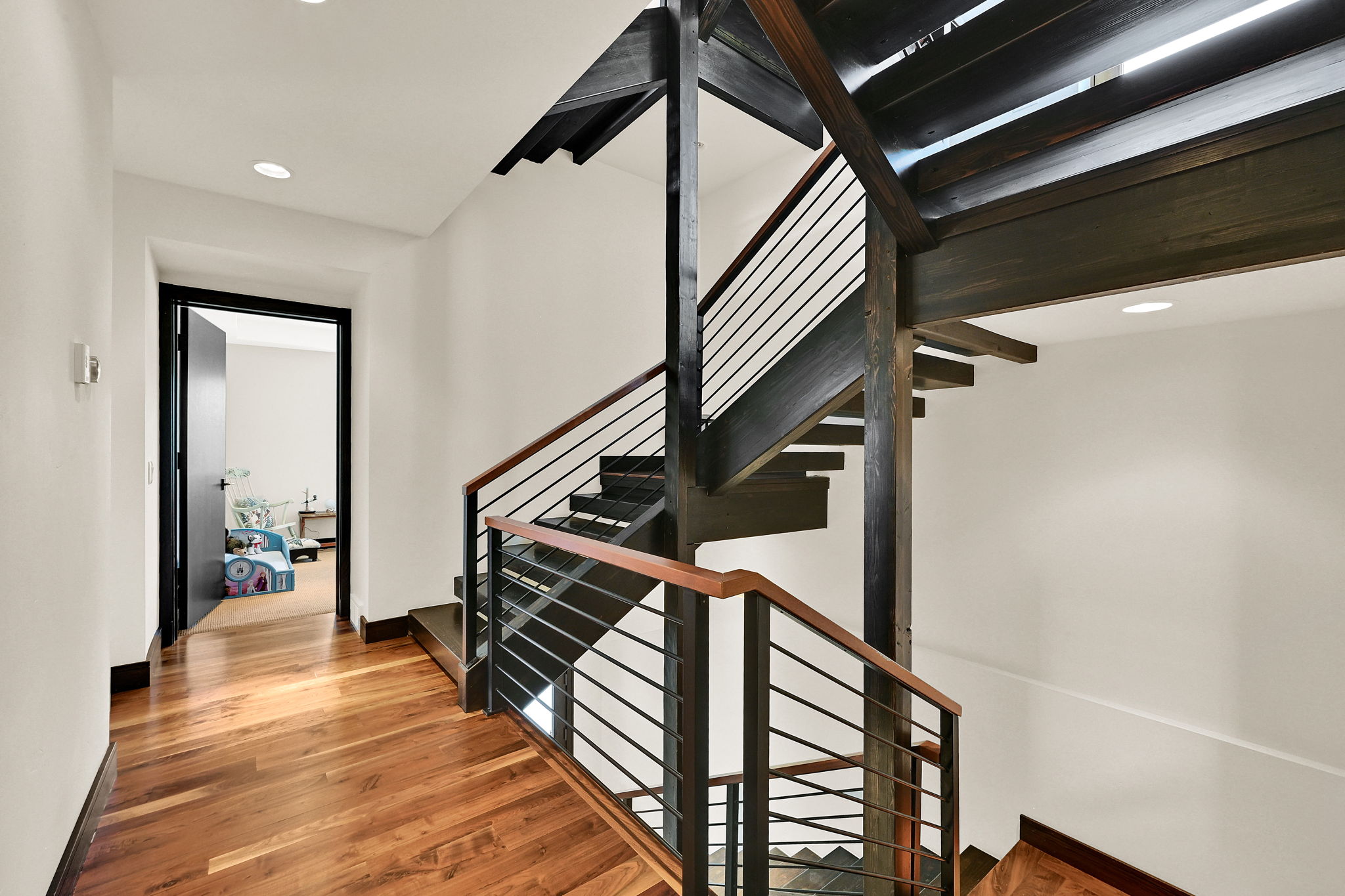 Contemporary staircase featuring dark-stained wood risers and stringers, complemented by a horizontal metal railing system and wood-finish handrails