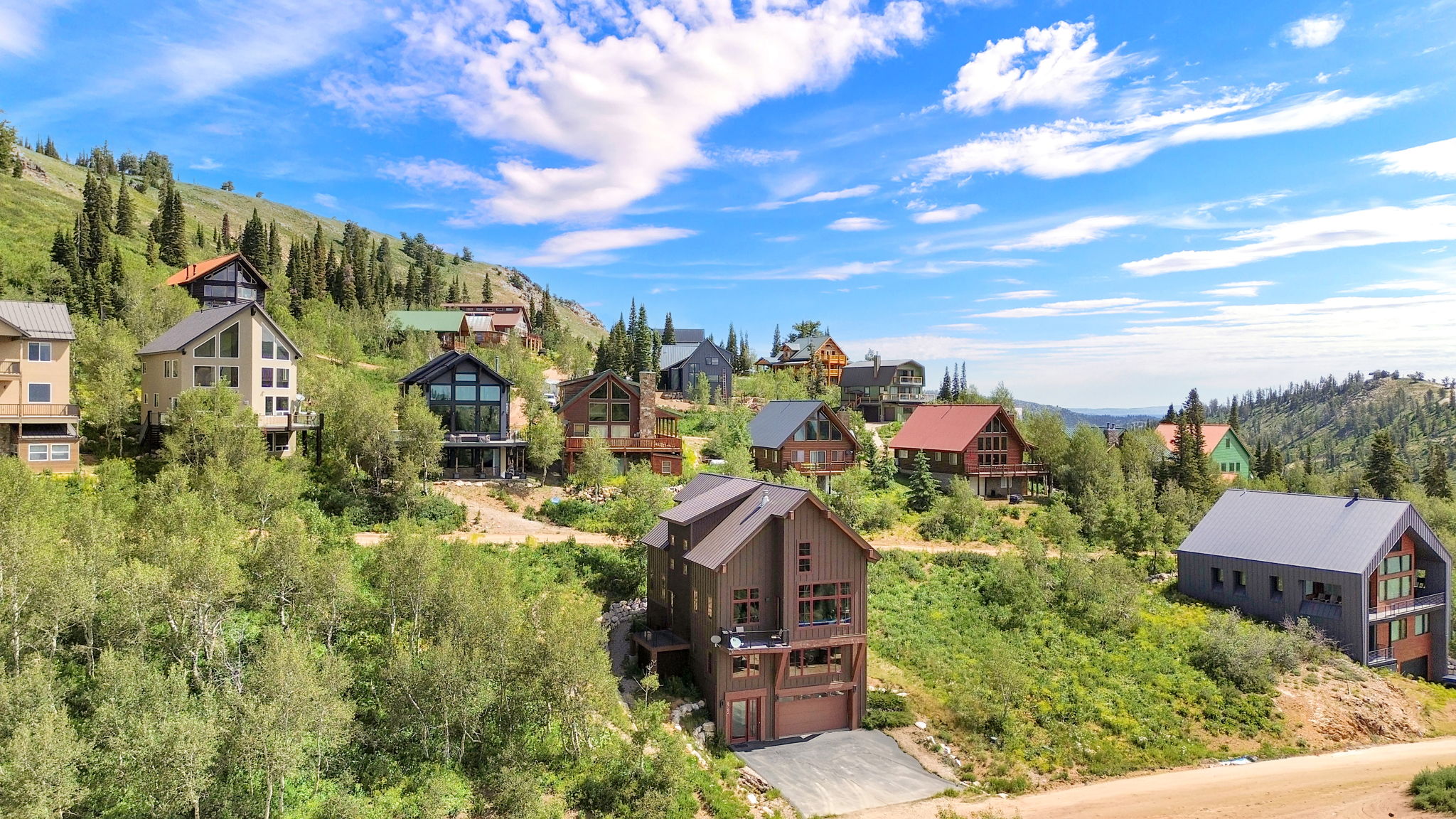 Mountain property featuring multiple residences on a hillside with natural landscaping, mature trees, and varying architectural styles