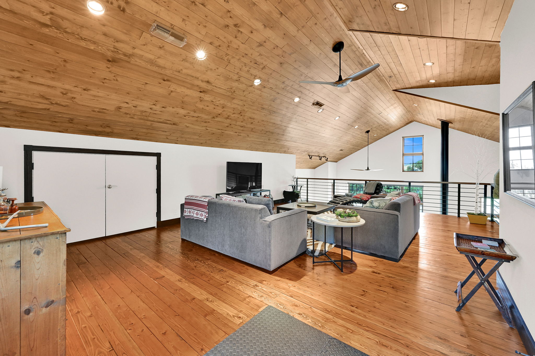 Spacious loft area featuring vaulted wood-paneled ceilings with recessed lighting, hardwood flooring, and a contemporary railing system