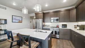 Kitchen with high end appliances, dark wood finished floors, dark wood finish cabinets, a kitchen island with sink, and a breakfast bar