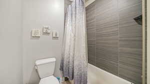 Bathroom featuring toilet and shower / bathtub combination with curtain