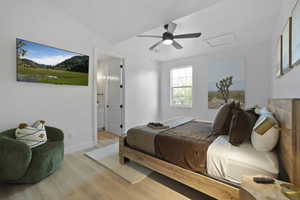 Bedroom featuring light wood finished floors, ceiling fan, ensuite bathroom, and vaulted ceiling