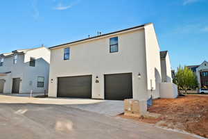 Back of house with an attached garage, concrete driveway, and stucco siding