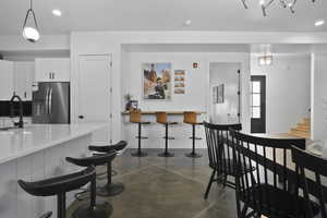 Kitchen with concrete flooring, white cabinets, a kitchen bar, stainless steel fridge, and hanging light fixtures