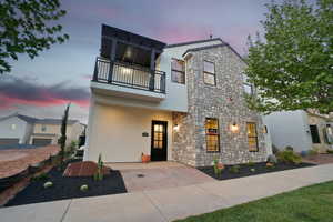 View of front facade featuring stone siding, stucco siding, and a balcony