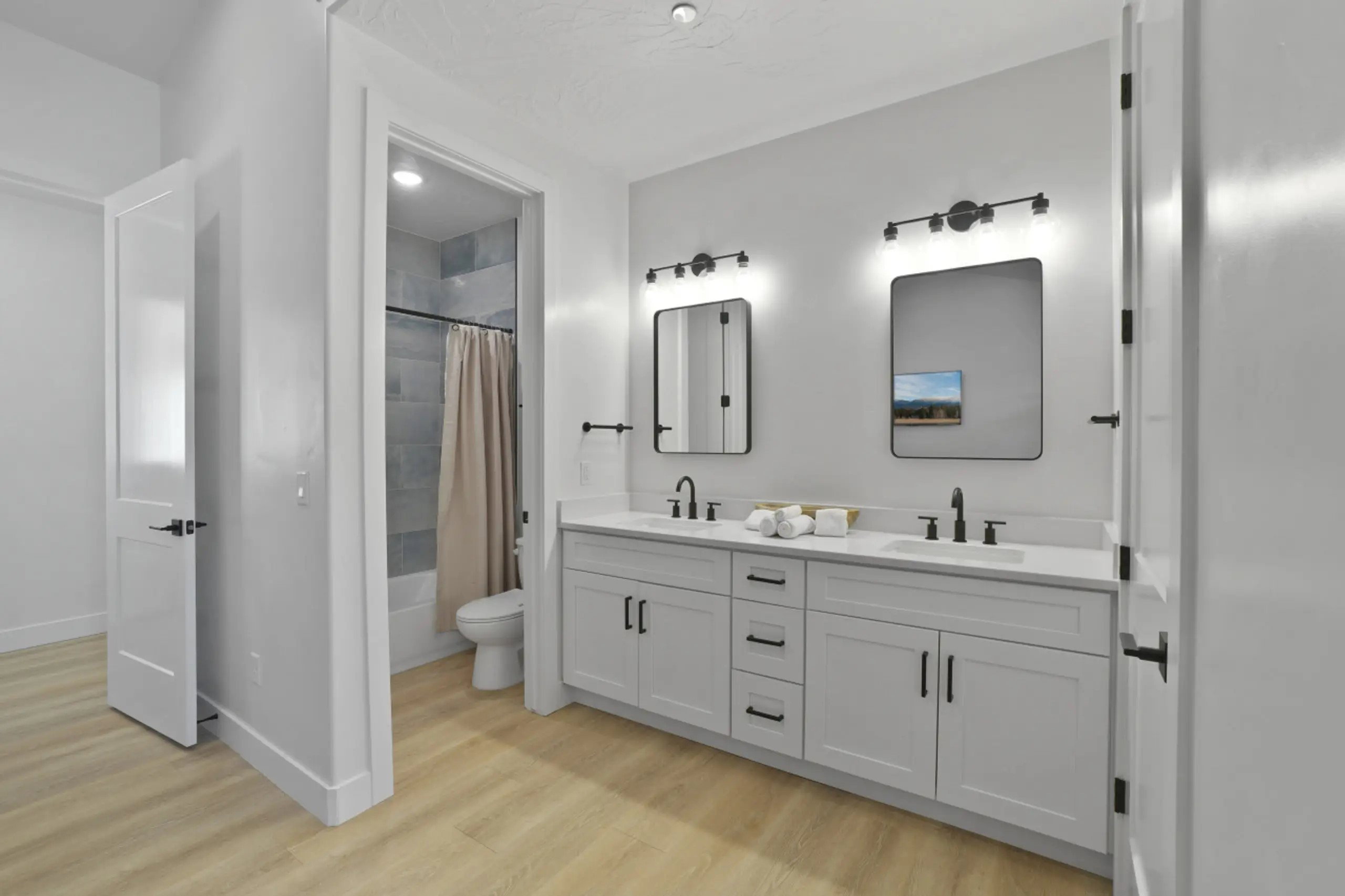 Bathroom with double vanity, light wood-style flooring, and shower / bath combo with shower curtain