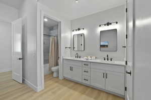 Bathroom with double vanity, light wood-style flooring, and shower / bath combo with shower curtain