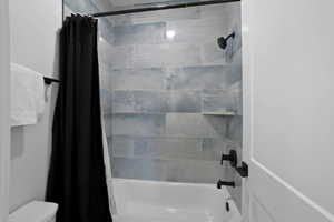 Bathroom with toilet and shower / bath combination with curtain