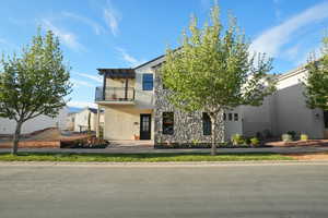 View of front of home featuring a balcony, stone siding, and stucco siding