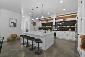 Kitchen featuring white cabinetry, finished concrete flooring, stainless steel appliances, and a kitchen island with sink