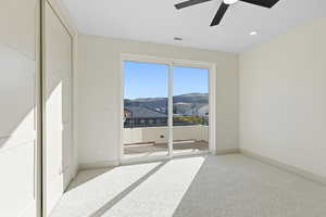 Unfurnished bedroom featuring light colored carpet, a mountain view, access to outside, and a ceiling fan