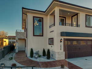 View of front of home with stone siding, stucco siding, an attached garage, a balcony, and concrete driveway