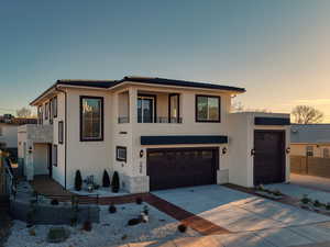 View of front facade featuring driveway, stucco siding, a garage, and a balcony