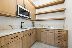 Kitchen featuring light stone countertops, white microwave, open shelves, and light stone finish flooring