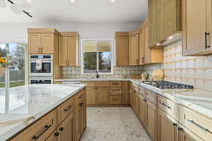 Kitchen with white double oven, light stone counters, tasteful backsplash, stainless steel gas stovetop, and recessed lighting