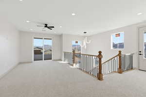 Carpeted empty room featuring a ceiling fan and suspended lighting