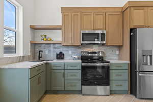 Kitchen with stainless steel appliances, open shelves, tasteful backsplash, and green cabinetry