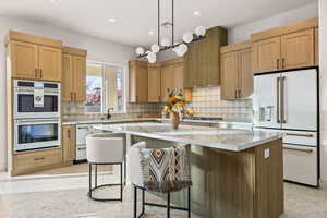 Kitchen featuring white appliances, a kitchen island, light stone counters, a kitchen bar, and hanging light fixtures