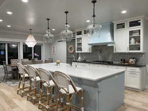 Kitchen featuring light wood-style flooring, a kitchen bar, glass fronted cabinets, a large island, and decorative light fixtures