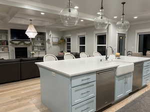 Kitchen featuring open floor plan, dishwasher, a kitchen island with sink, a fireplace, and coffered ceiling