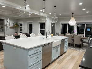 Kitchen featuring a kitchen island with sink, stainless steel dishwasher, light wood-type flooring, a kitchen bar, and light stone counters