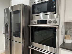 Kitchen view of stainless steel appliances, white cabinets, and backsplash