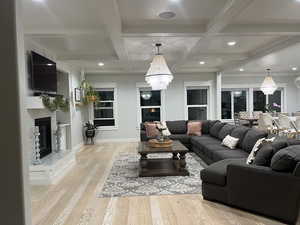 Living area featuring a chandelier, a glass covered fireplace, light wood-type flooring, and coffered ceiling