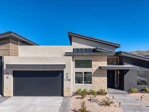 Contemporary house with stone siding, an attached garage, driveway, and stucco siding