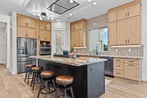 Kitchen with light stone counters, stainless steel appliances, light wood finish cabinetry, a center island, and recessed lighting