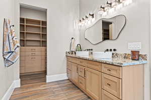 Bathroom featuring double vanity, a walk in closet, and light wood-style floors