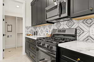 Kitchen featuring stainless steel appliances, light stone counters, dark cabinets, decorative backsplash, and recessed lighting