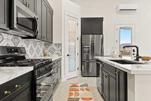 Kitchen featuring stainless steel appliances, light stone countertops, a kitchen island with sink, and dark cabinetry