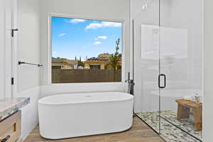Full bathroom featuring wood finished floors, a stall shower, tile walls, a freestanding tub, and plenty of natural light