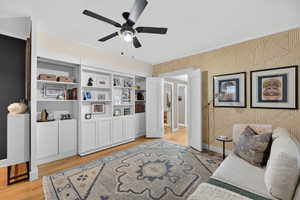 Room featuring extensive built-in white cabinetry and shelving, hardwood flooring, and a ceiling fan with light fixture