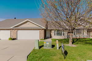Single story home featuring brick siding, concrete driveway, an attached garage, and a front yard
