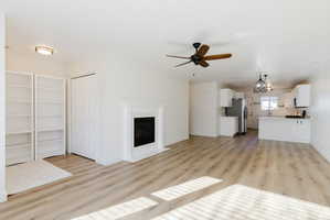 Unfurnished living room with a ceiling fan, light wood finished floors, suspended lighting, and a fireplace