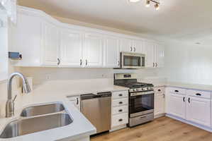 Kitchen with stainless steel appliances, white cabinetry, light wood-type flooring, and a textured ceiling