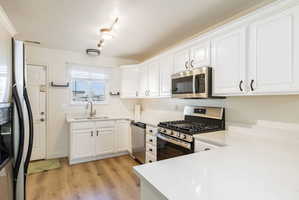Kitchen featuring stainless steel appliances, white cabinetry, light wood-type flooring, a textured ceiling, and light stone countertops
