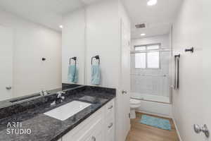 Bathroom with vanity, bath / shower combo with glass door, and light wood-style floors