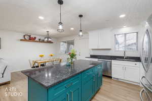 Kitchen featuring dual tone cabinets, light wood-style floors, stainless steel appliances, dark stone counters, and pendant lighting