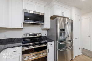 Kitchen featuring stainless steel appliances, white cabinetry, dark stone countertops, and light wood finished floors