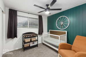 Carpeted bedroom with a crib, ceiling fan, and wood walls