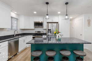 Two tone kitchen with a kitchen breakfast bar, stainless steel appliances, a center island, dark stone counters, and two tone cabinets