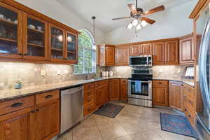 Kitchen featuring stainless steel appliances, wood finish cabinetry, lofted ceiling, and decorative light fixtures