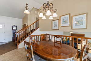 Dining space with vaulted ceiling, light carpet, light tile patterned flooring, and a chandelier