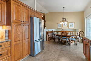Kitchen with wood finish cabinetry, light stone countertops, freestanding refrigerator, vaulted ceiling, and light tile patterned flooring