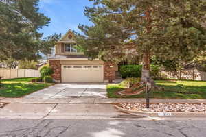 View of property hidden behind natural elements with driveway, brick siding, and a garage