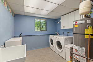 Laundry room featuring strapped water heater, a paneled ceiling, independent washer and dryer, cabinet space, and light flooring
