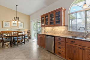 Kitchen featuring vaulted ceiling, glass fronted cabinets, wood finish cabinetry, light stone countertops, and stainless steel dishwasher