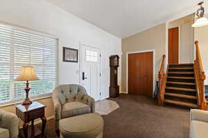 Carpeted living room featuring stairway and lofted ceiling
